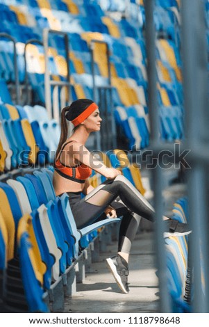 side view of attractive young woman sitting on tribunes at sports stadium