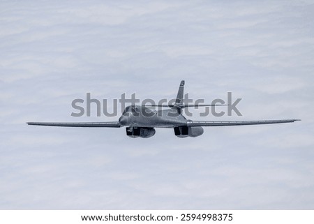 Side  view of a B-1 Lancer among clouds, with wings full forward