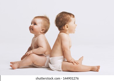 Side view of babies sitting back to back on white background