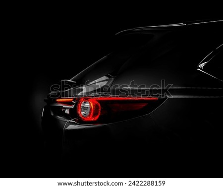 Side view of the back of a black car on a dark background with a close-up of the headlights