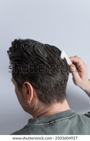 Side view from the back of the head of a man combing his gray hair with a comb. Copy space. Isolated on gray background. Hair styling and hair care concept