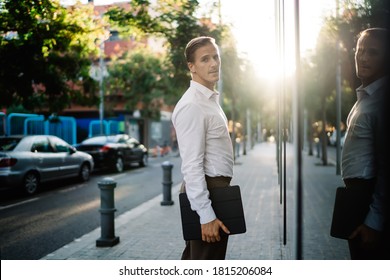 Side View Of Backlit Youthful Entrepreneur In Formal Wear Holding Tablet On Narrow Pavement During Daytime And Looking Over Shoulder At Camera