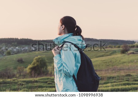 Side view of the backpacker standing on the green hill and looking on the horizon. Concept of the travelling, backpacking, hiking, outdoor recreation, success, inspiration,