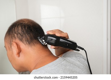 Side View Of Bald Asian Male Self Haircut With Clippers Indoor.