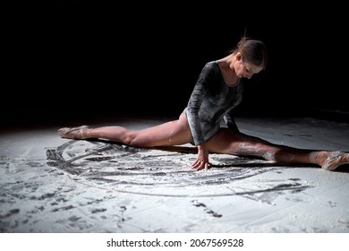 Side view ballet dancer sitting floor in ballet pose with flour. young caucasian woman ballerina posing on black studio background, stage, performance. flexible female is dressed in black bodysuit