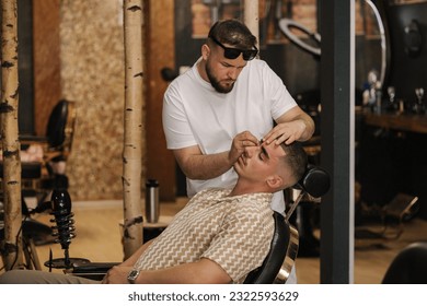 Side view of barber man trimming eyebrows with tweezers for confident man - Powered by Shutterstock
