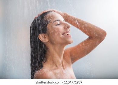 Side view beaming lady locating under stream of water. She holding hair with arms