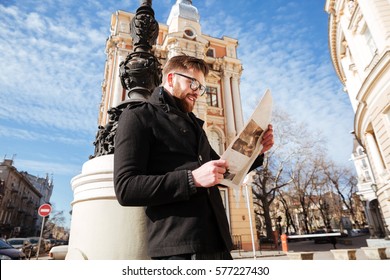 Side view of Bearded Man in coat and eyeglasses reading newspaper on the street