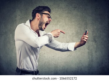 Side View Of Bearded Man In Glasses Holding Smartphone And Yelling At It Being Rude. 