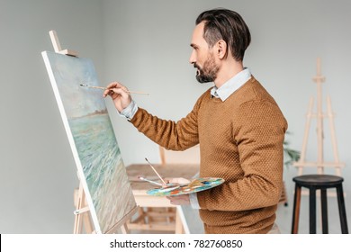 side view of bearded man painting on easel at art class