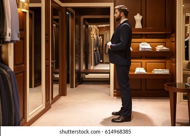 Side view of bearded man which tries on a suit while being in a shop. Full  length portrait