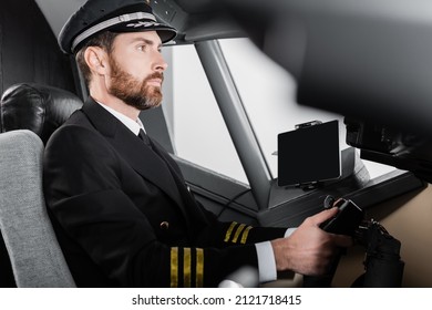 Side View Of Bearded Pilot In Uniform Using Yoke In Airplane