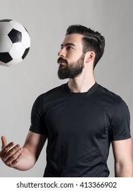 Side View Of Bearded Young Football Or Soccer Player Throwing Ball Over Gray Studio Background.