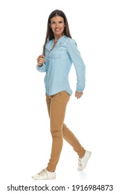 Side View Of A Beautiful Casual Woman Walking One Way And Looking At The Camera Against White Background