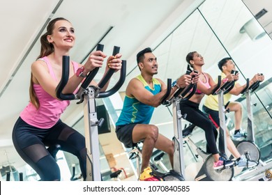 Side view of a beautiful fit young woman smiling while pedaling during cardio workout at indoor cycling group class in a modern fitness club 