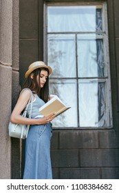 side view of beautiful girl in hat holding paper cup and reading book
