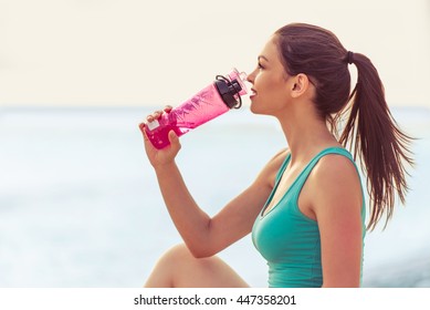 Side view of beautiful girl in sport clothes drinking water after workout on the beach