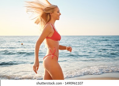 Side view of beautiful smiling blond woman in swimsuit happily walking by the sea