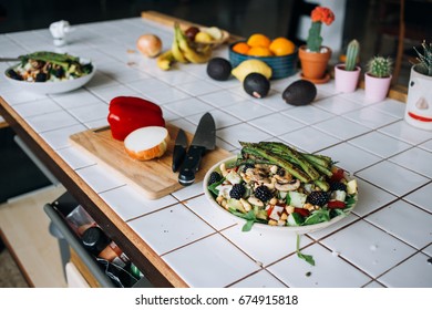 Side view of beautiful tiled kitchen island counter, with fresh ingredients, cutting board and bowl of vegan raw vegetables salad full of berries and tasty snacks