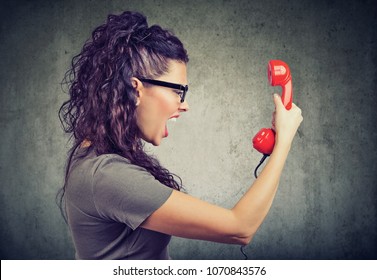 Side View Of Beautiful Woman Holding A Red Telephone Receiver And Yelling In Anger. 