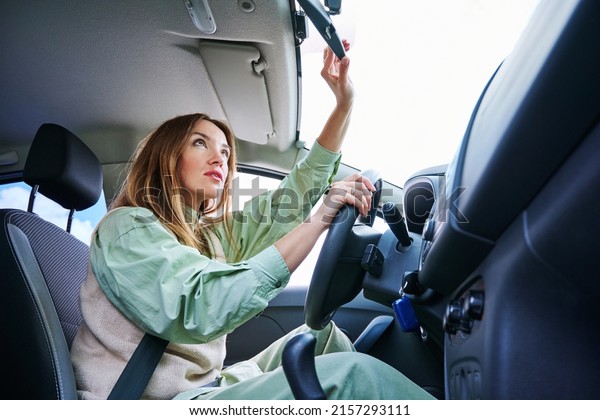 Side view of beautiful woman touching\
rearview mirror and smiling while driving\
car