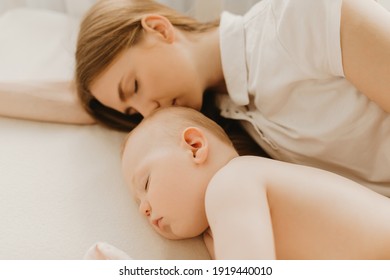 Side view of beautiful young mother and her cute little baby sleeping in bed at home