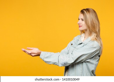 Side View Of Beautiful Young Woman In Denim Casual Clothes Holding Something In Her Hands Isolated On Bright Yellow Orange Wall Background In Studio. People Lifestyle Concept. Mock Up Copy Space