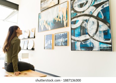Side view of a beautiful young woman studying and watching the abstract paintings and colorful canvases during a visit to the art gallery 