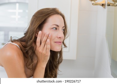 Side view of a beautiful young woman examining her face in the bathroom at home - Powered by Shutterstock