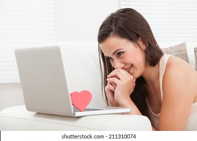 Side view of beautiful young woman dating online on laptop at home