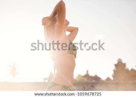 side view of beautiful young woman in bikini playing with hair with sunlight on background