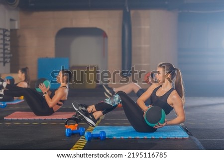 Side view of beautiful young women exercising russian twist with medicine ball from sitting position for strong abs