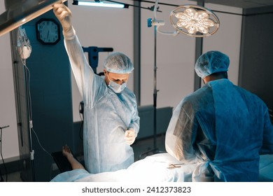 Side view of being operated by professional surgeons. Male doctor adjusting light performing operation wearing medical gown. Surgeon adjusting surgical lamp before operation. Concept of emergency. - Powered by Shutterstock