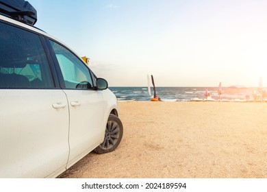 Side View Of Big Family White Suv Van Car With Big Rooftop Cargo Rack Box At Scenic Sand Seaside Campsite Camp Coast Of Sea Or Ocean Sky On Background. Accessory Rental Travel Trip Vacation Concept