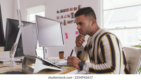 Side view of a biracial man working in a creative office, using computer, graphic tablet and laptop computer at his office - Powered by Shutterstock