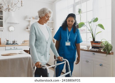 Side view of black african american nurse volunteer teaching elderly woman with gray hair in cardigan to use walker, supporting her and giving advice and instructions, standing in her kitchen - Powered by Shutterstock