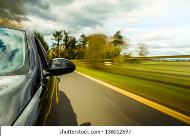 Side View Of Black Car Driving On The Country Road.