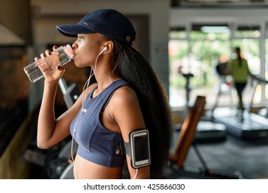 Side View Of Black Female Athlete Drinking Water From Bottle In The Gym