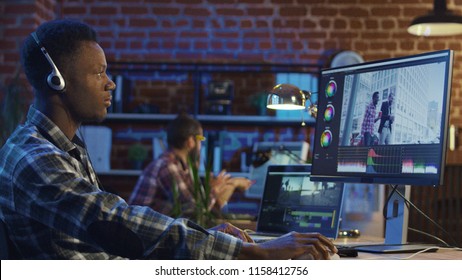 Side view of black man in headphones working on computer and editing video with color correction