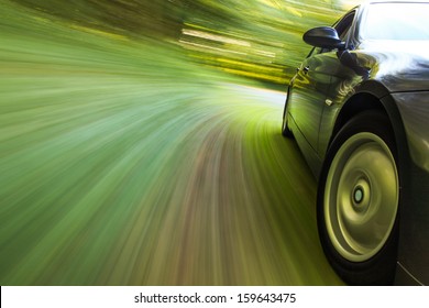 Side View Of Black Sedan Driving In Forest.