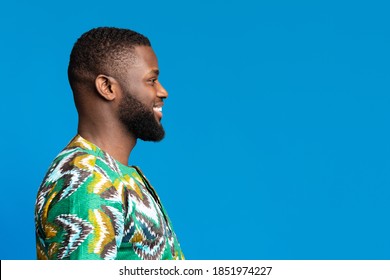 Side View Of Black Smiling Guy In African Shirt Looking At Free Space On Blue, Studio Shot, Panorama. Excited African American Young Man Staring At Great Deal Or Offer Over Colorful Background