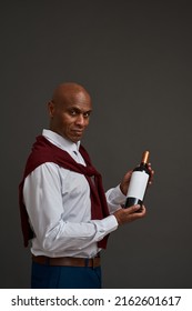 Side view of black winemaker or sommelier holding wine bottle. Adult successful male entrepreneur looking at camera. Viticulture and winemaking. Isolated on grey background. Studio shoot. Copy space - Shutterstock ID 2162601617