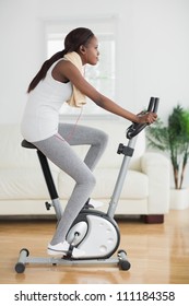 Side View Of A Black Woman Doing Exercise Bike In A Living Room