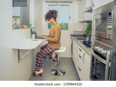 Side view of a black woman working at home during Coronavirus quarantine.  Conference call in the kitchen wearing pajamas and jacket. - Shutterstock ID 1709844310