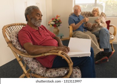 Side view of blind senior man reading a braille book on chair while senior couple using digital tablet at nursing home - Powered by Shutterstock