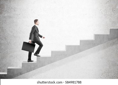 Side View Of A Blond Man In A Suit Climbing Stairs Against A Concrete Wall. Concept Of A Road To Success In Business. Mock Up