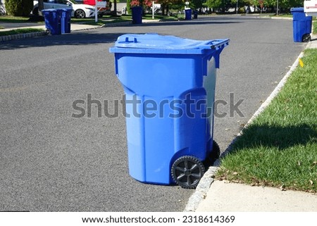 Side view of a blue recycling bin on an asphalt street near a curb