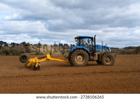 A side view of a blue tractor pulling a yellow plough