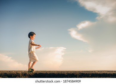 Side View Of The Boy Keeping His Balance To Walk Straight Down The Path. He Is Enjoying The Outdoors In The Evening.