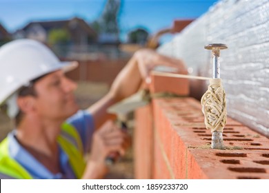A side view of bricklayer setting bricks on a wall in alignment with line pins and thin rope in selective focus